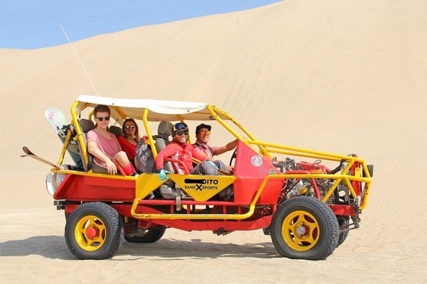 Een buggy met passagiers, een woestijnlandschap en zandduinen op de achtergrond. 2