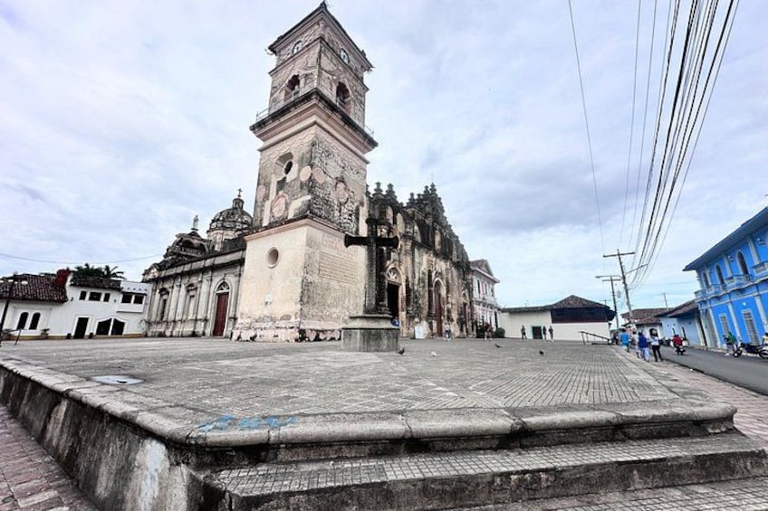 A historic church with a bell tower, a paved square, and a blue building in the background. 3