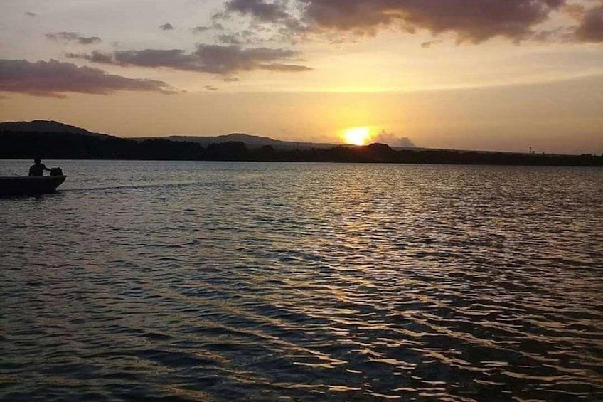 A sunset over a body of water with a silhouette of a boat and distant hills. 2