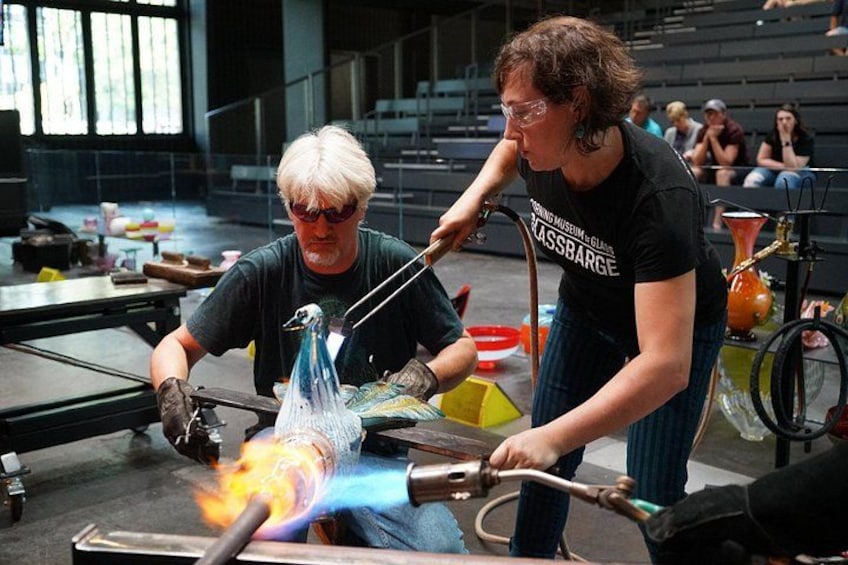 Two people working with a glass sculpture, a table, and a window in the background. 2