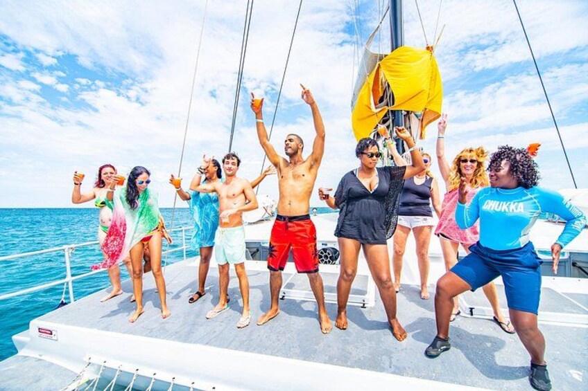 A group of people on a sailboat with a yellow canopy, ocean in the background. 2