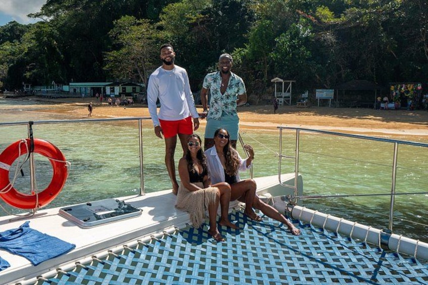 A group of people on a boat with a lifebuoy, a checkered mat, and a beach in the background. 3
