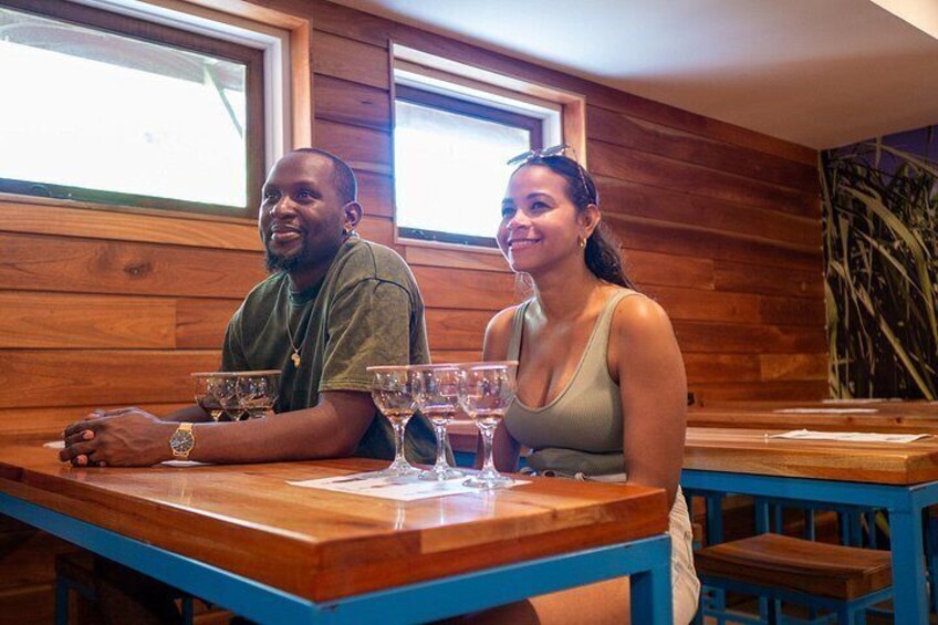 Dos personas sentadas en una mesa de madera con una copa de vino, en una habitación con paredes y ventanas de madera. 3