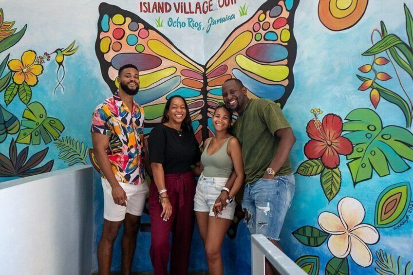 Un mural con una mariposa y flores tropicales, y el texto 'Island Village Out'. 2