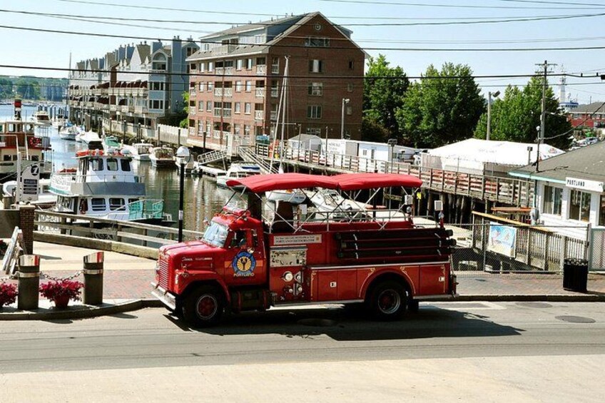 A red fire truck parked by a waterfront with boats and buildings in the background. 1