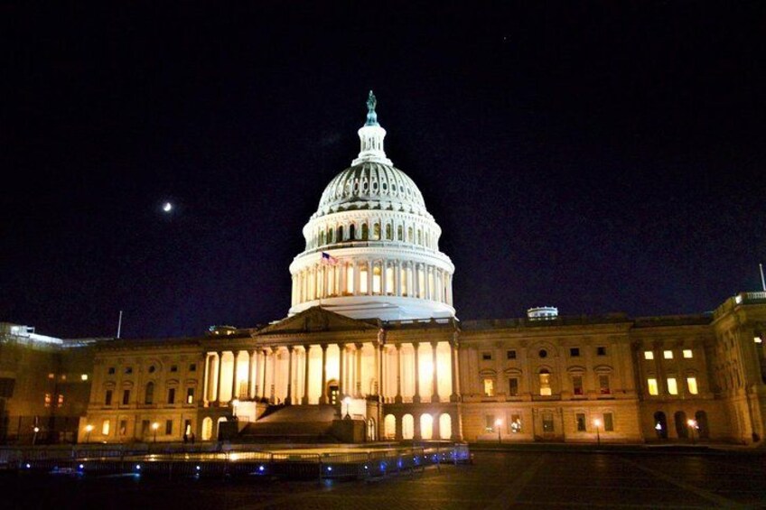 A large, illuminated capitol building at night with a moon in the sky. 5
