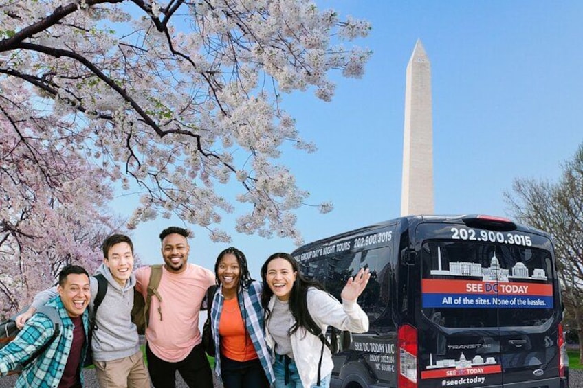 En gruppe mennesker står foran en bus, med Washington Monument i baggrunden. 3