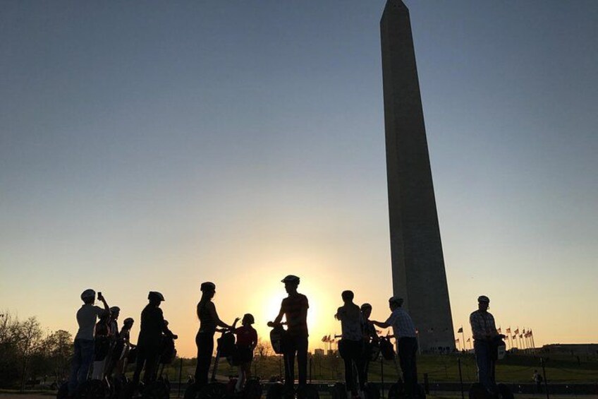 A group of people standing in a line, facing a tall monument, with the sun setting in the background. 3