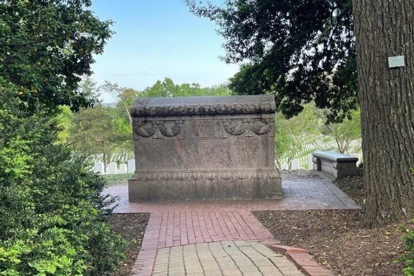 A stone monument with intricate carvings, surrounded by trees and a paved walkway. 4