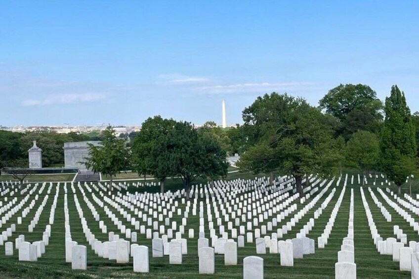 A cemetery with rows of white headstones, a monument, and the Washington Monument in the background. 5