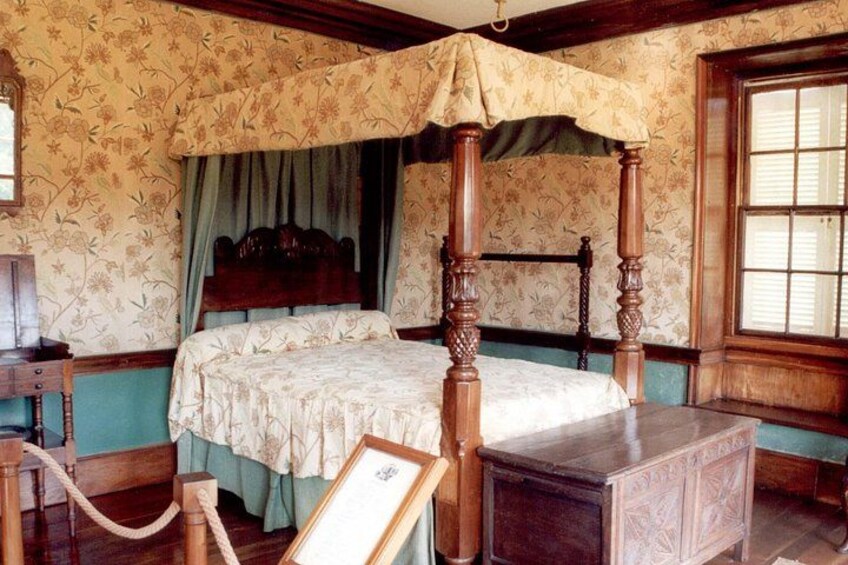 A four-poster bed with a canopy, a wooden nightstand, and a framed picture on the floor. 4