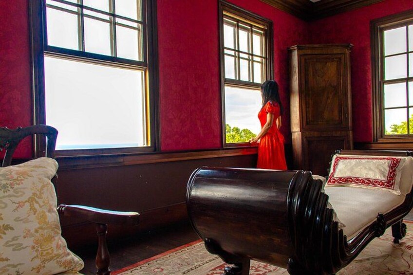 A room with red walls, a large window, a wooden cabinet, and a vintage armchair. 3
