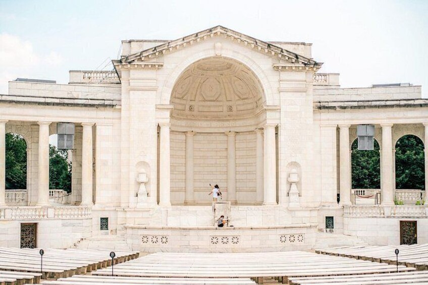 A large neoclassical building with a central archway, flanked by columns, and a wide open plaza in front. 1