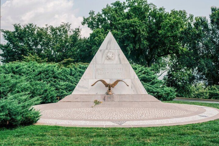 Ein dreieckiges Denkmal mit einer Adlerstatue, umgeben von einem Rundgang und Grünflächen. 2