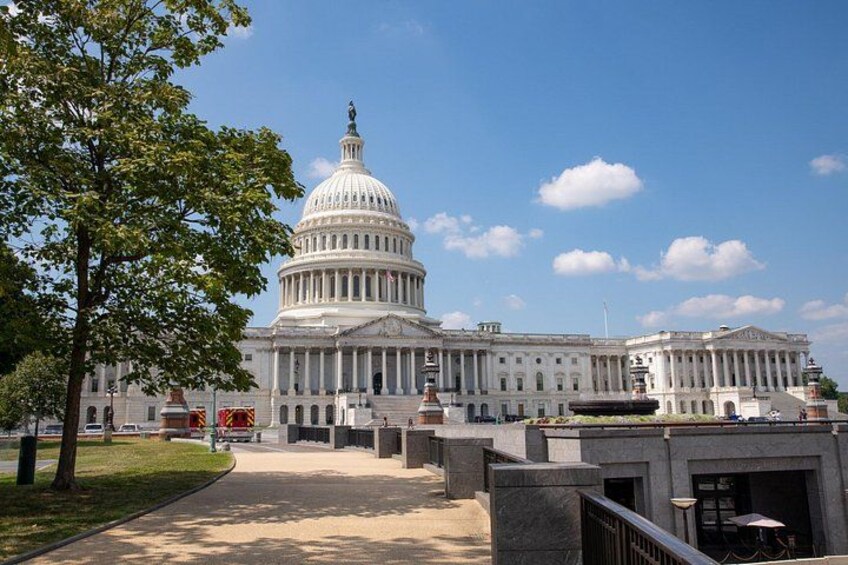 A large white capitol building with a dome, surrounded by a paved walkway and a tree. 3
