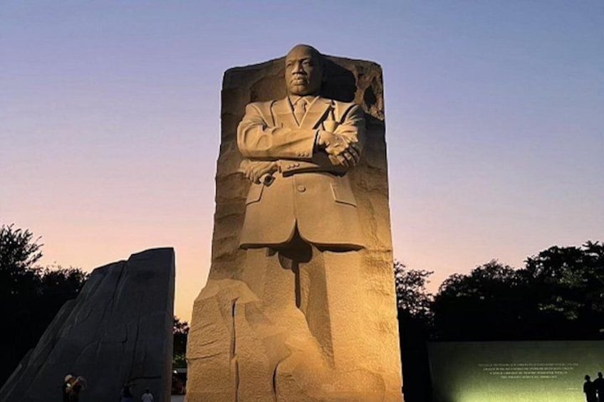 A large stone monument with a figure in a suit, a large open space, and a clear sky. 2