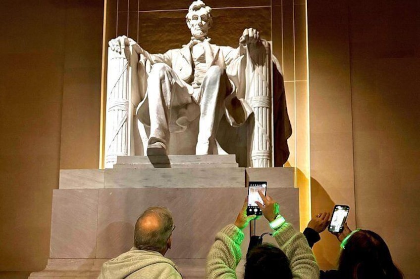 A statue of a seated man with a smartphone in hand, surrounded by people. 2
