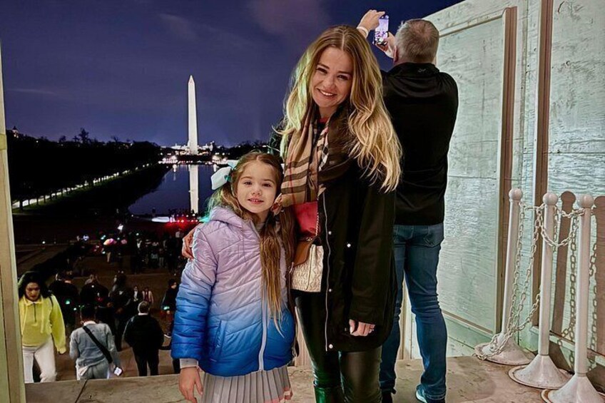A person taking a photo with a smartphone, a child in a blue jacket, and a monument in the background. 4