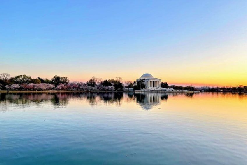 A calm lake with a reflection of a white dome-shaped building, surrounded by trees and a clear sky. 5