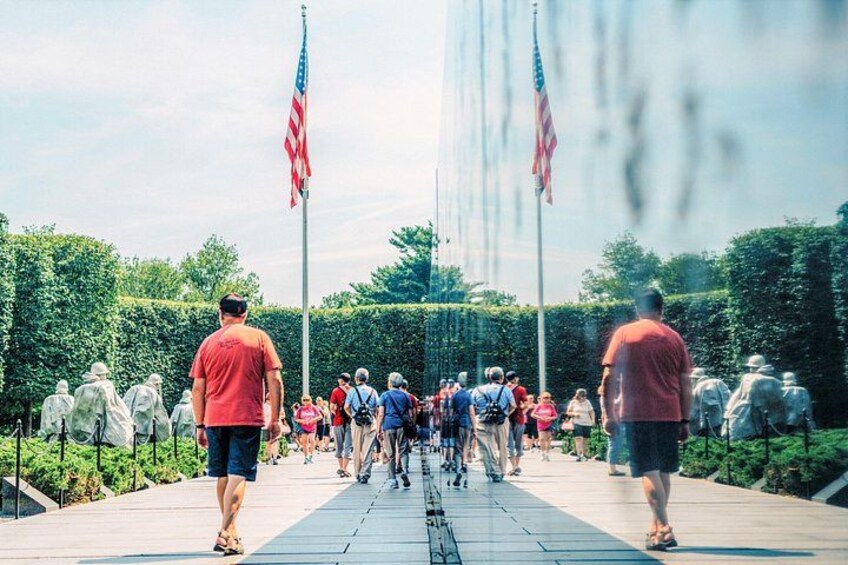 Een groep mensen loopt over een verhard pad, omringd door groen, met Amerikaanse vlaggen op stokken. 4