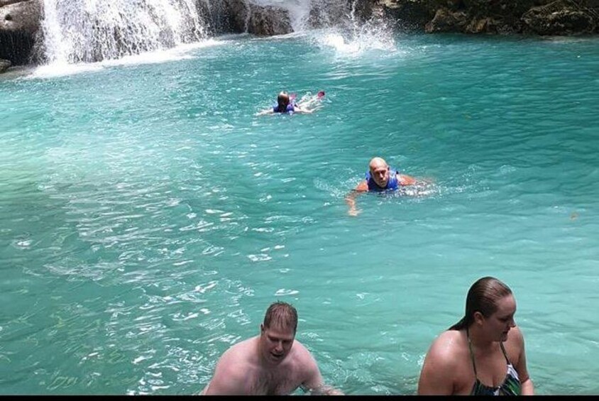 A waterfall, clear turquoise water, and people swimming. 2