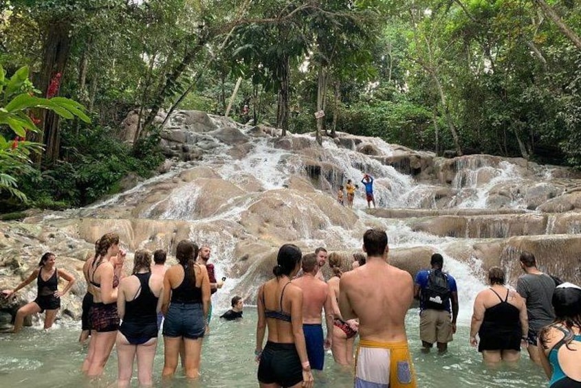A waterfall in a forested area with people standing and walking around. 3