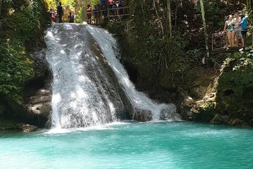 A waterfall cascading into a turquoise pool surrounded by lush greenery. 1