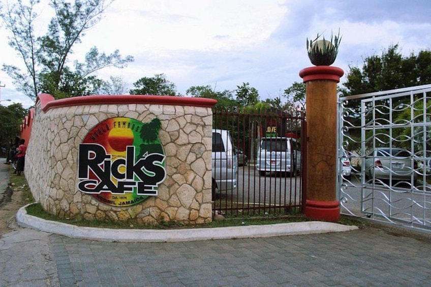 Un muro de piedra con un cartel que dice Rick's Cafe, una reja metálica y un coche estacionado. 2