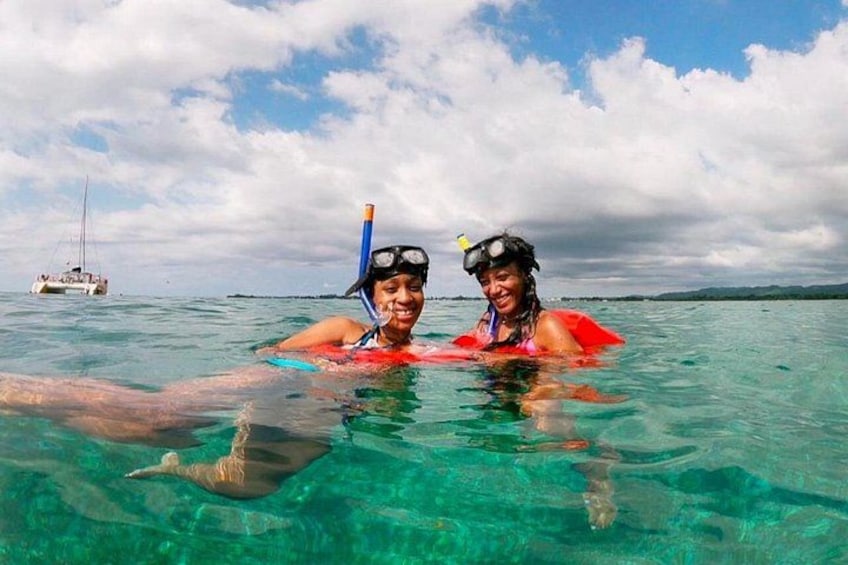 Dos personas haciendo snorkel en aguas azul turquesa, con un bote al fondo. 3