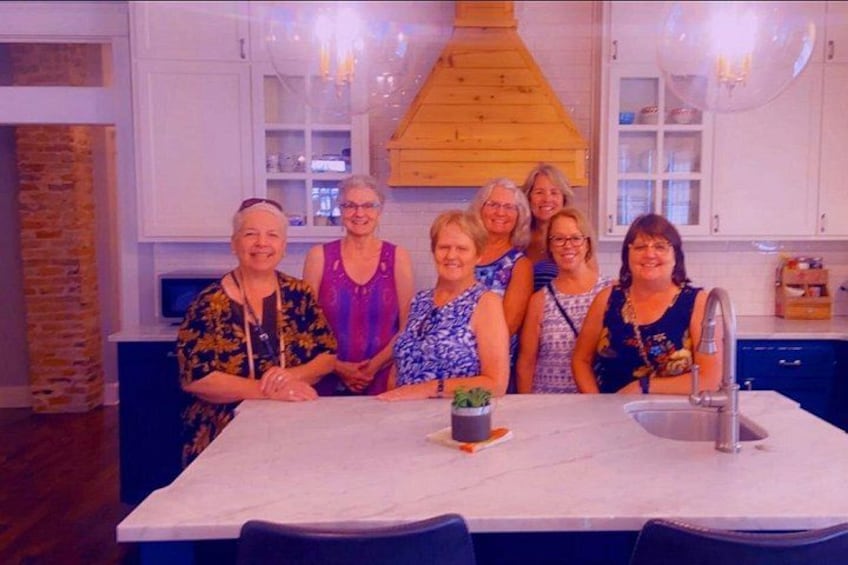 A group of people seated at a kitchen island with a potted plant, a sink, and a wooden hood above the stove. 4