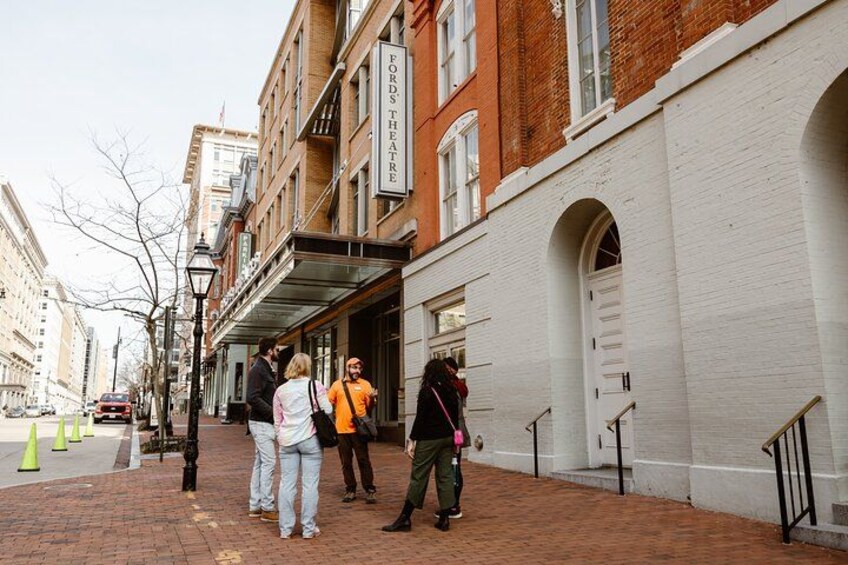 A group of people standing on a brick sidewalk in front of a theater. 1