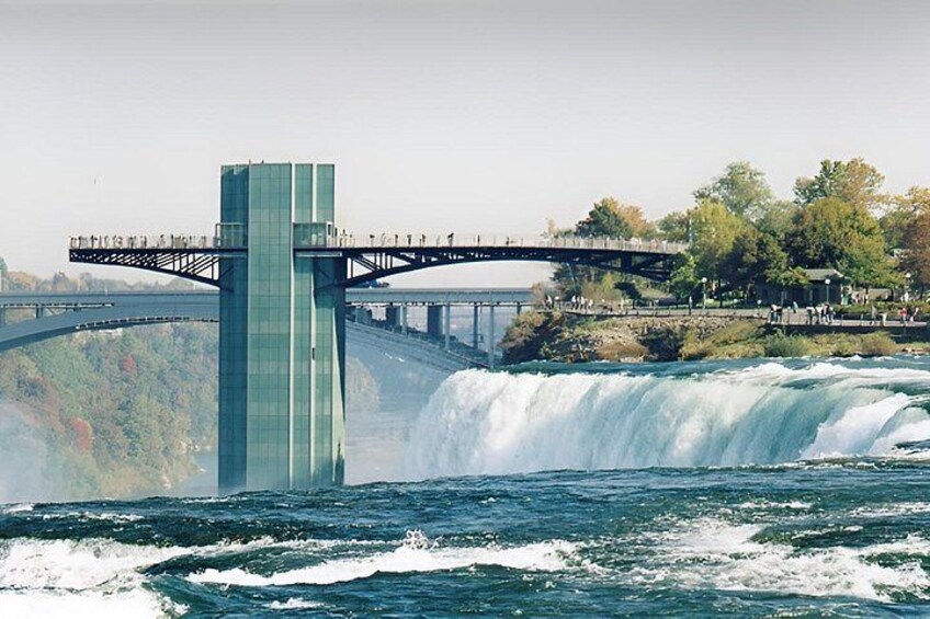 Een brug over een waterval, met een torenstructuur en mensen op de brug. 5