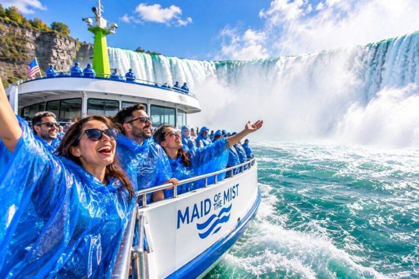 Een boot met mensen in blauwe regenponcho's, een grote waterval op de achtergrond en de tekst 'MAID OF THE MIST' op de zijkant van de boot. 1