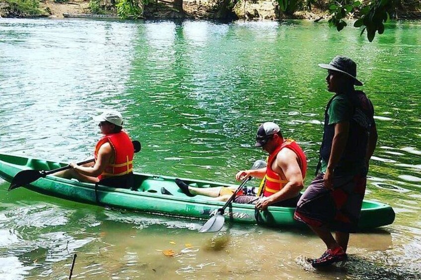 Twee personen in een groene kano op een rivier, met zwemvesten. 4