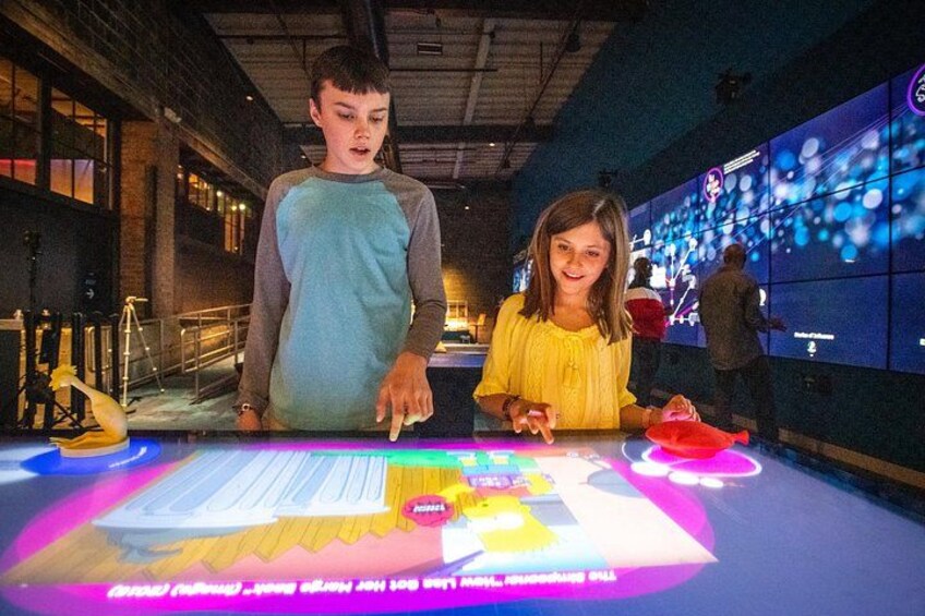 Twee personen die een digitaal display aanraken in een binnenruimte. 2