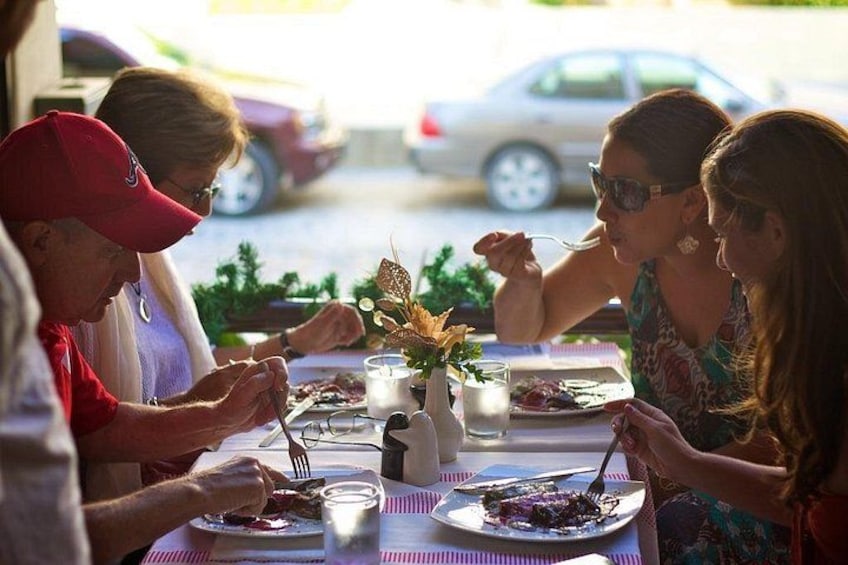 A group of people dining at an outdoor table with plates of food, glasses, and a candle. 3