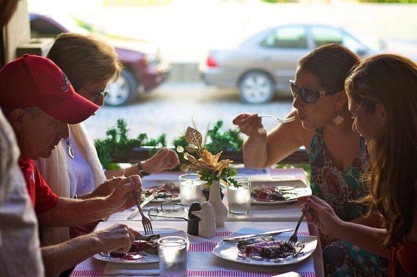 A group of people dining at an outdoor table with plates of food, a vase with flowers, and a candle. 2