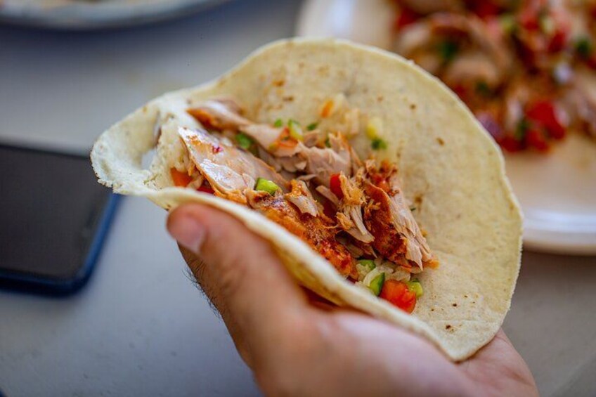A hand holding a taco with shredded meat, diced tomatoes, and green onions. 2