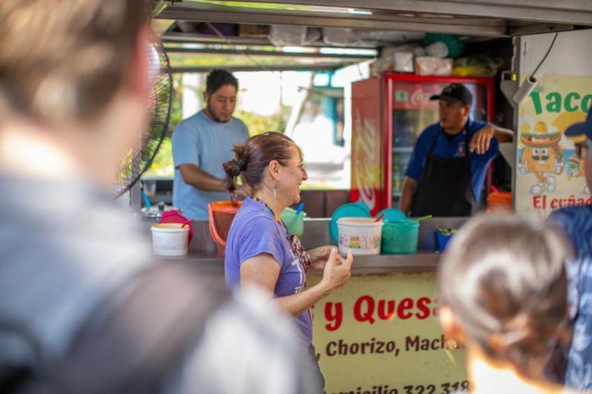 A street food vendor with a sign reading 'Taco y Queso' and a Coca-Cola refrigerator in the background. 3