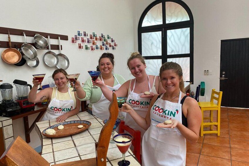 Four people in a kitchen, wearing aprons with 'COOKIN' printed on them, holding drinks and a plate. 2