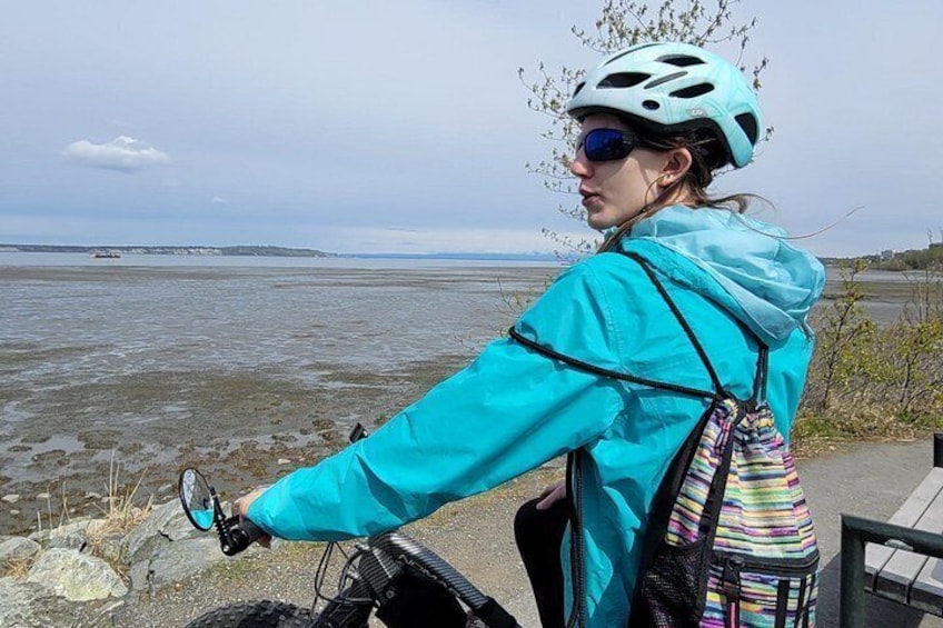 A person on a bicycle with a helmet, wearing a blue jacket, near a body of water. 2