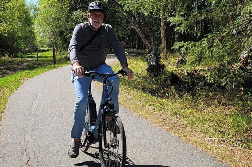 A person riding a bicycle on a paved path surrounded by trees. 5