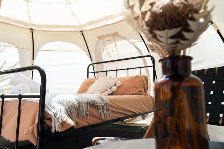 Ein gemütliches Zelt mit einem Bett, einer Vase mit getrockneten Blumen und einem schwarzen Metallgestell. 4