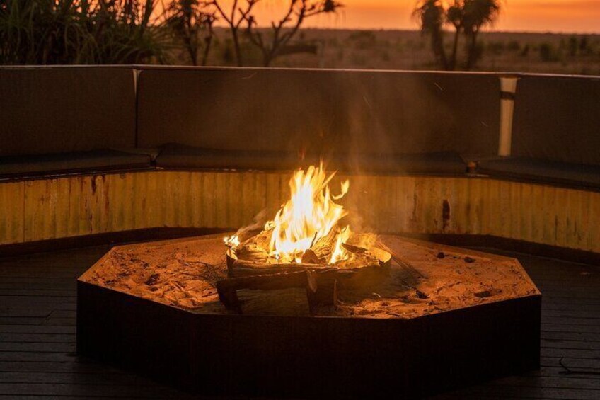 A circular fire pit with flames on a wooden deck at sunset. 5