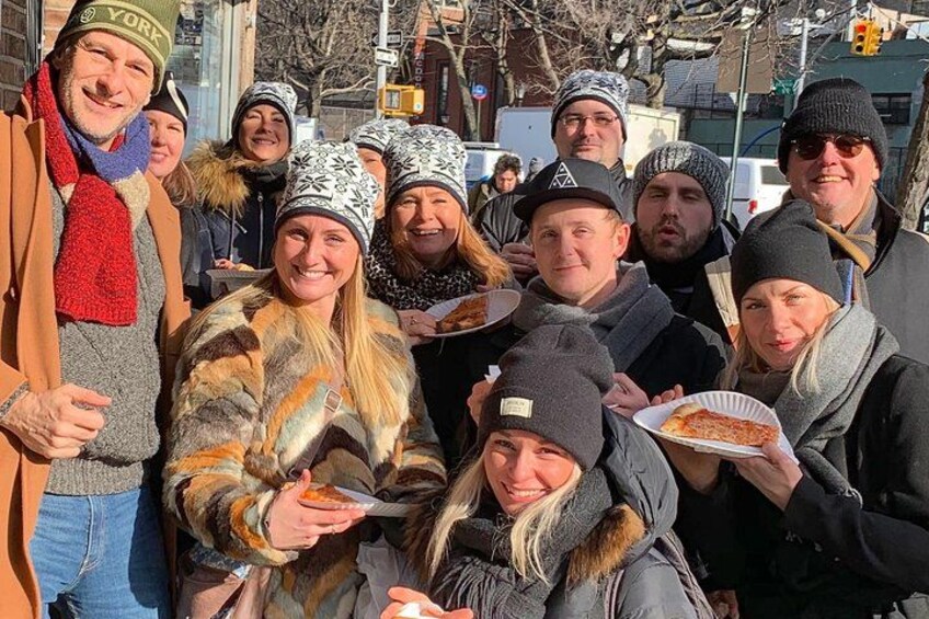 A group of people outdoors, some holding food, with buildings and trees in the background. 2
