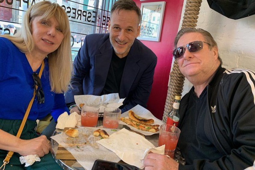 Three people sitting at a table with food and drinks. 3