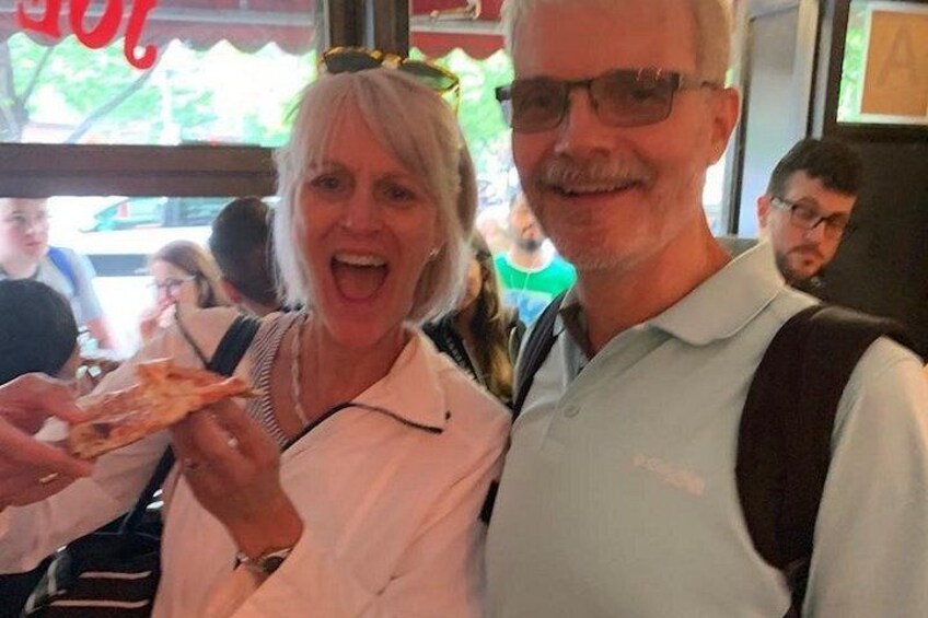 Two people holding a slice of pizza in a restaurant. 2