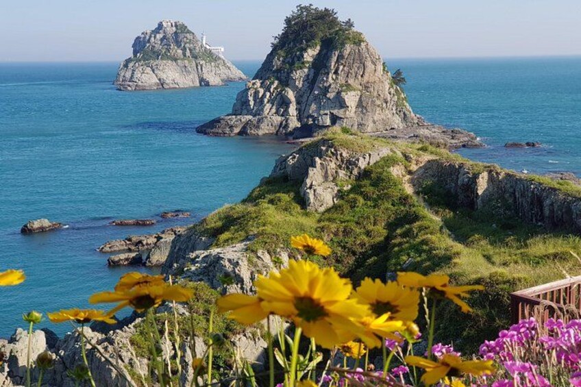 A coastal landscape with rocky cliffs, a lighthouse, and vibrant wildflowers. 2