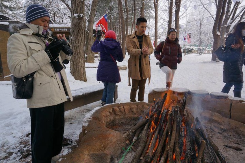 Eine Gruppe von Menschen versammelt sich um ein Lagerfeuer in verschneiter Landschaft. 3