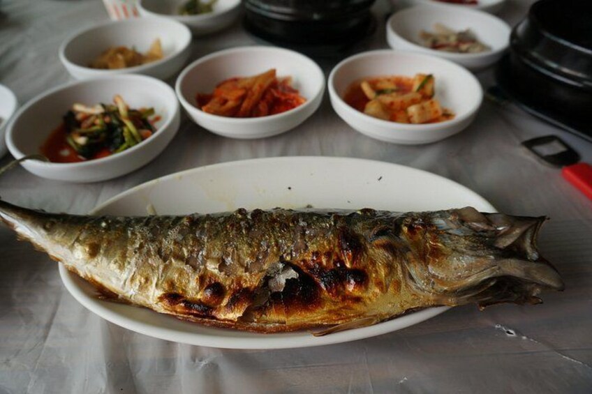 A whole grilled fish on a plate with several small bowls of side dishes in the background. 2